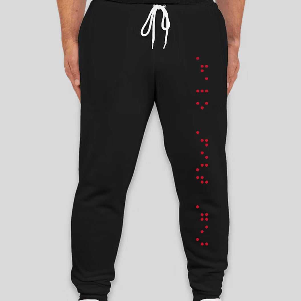 The image shows a pair of black joggers with a white drawstring at the waist. A vertical line of red Braille dots runs down the right leg, reading "Halo Fight Gear."