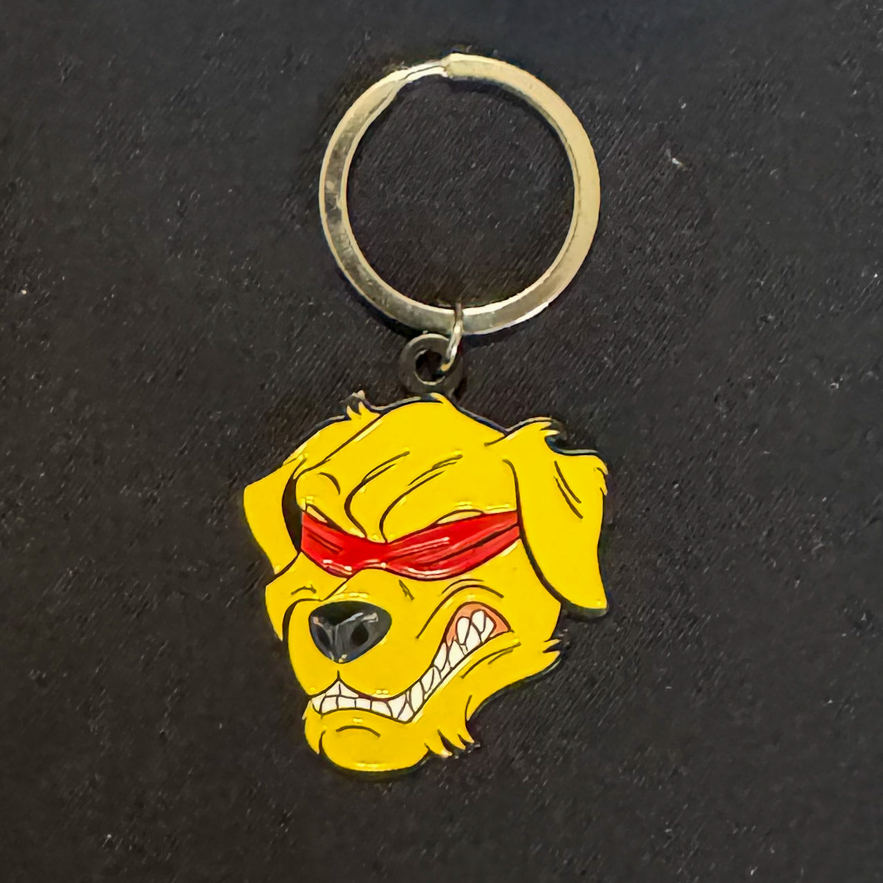 The image shows a keychain featuring the Halo Fight Gear logo. The keychain displays a fierce golden retriever with bared teeth, wearing a red blindfold. It is attached to a metal ring on a black background.