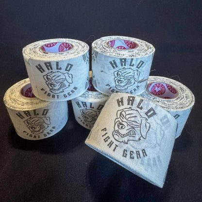 The image features six rolls of white athletic tape with a printed design. The design includes the text "HALO FIGHT GEAR" and a logo of a fierce dog wearing a blindfold. The rolls are arranged on a dark surface, with red and white patterns visible on the inner cores.